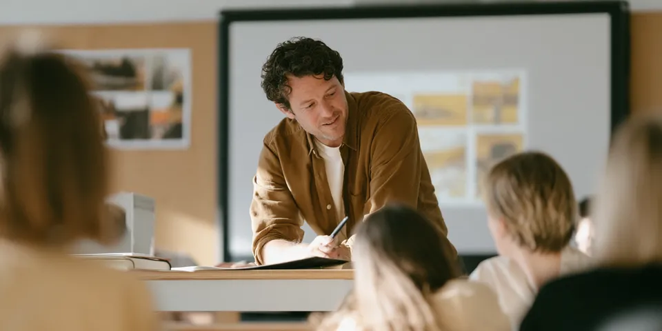 A teacher leaning over a desk to help a student in a classroom